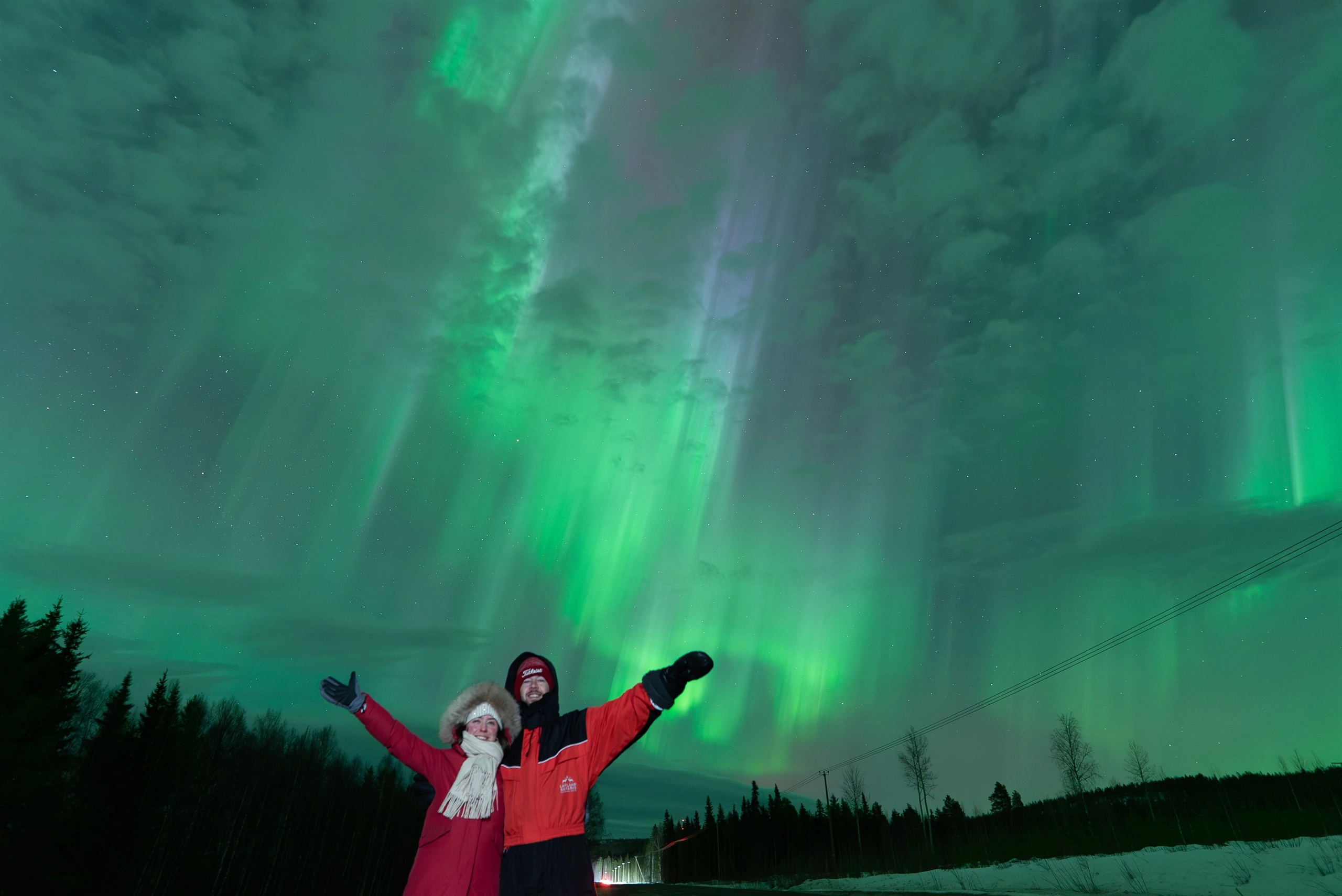 Guests with arms raised under an aurora corona in Lapland