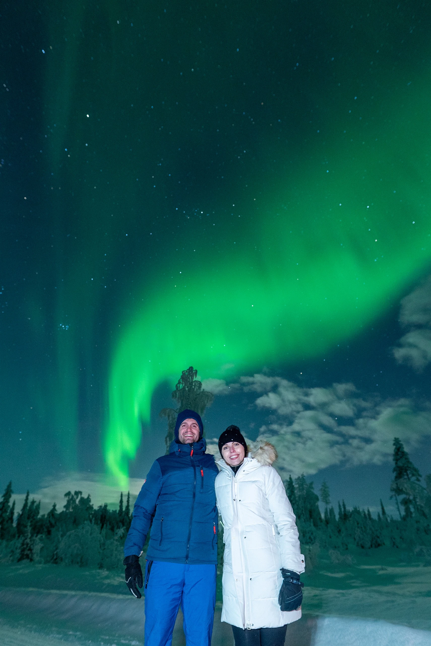 Couple smiling under a bright aurora swirl in Finnish Lapland