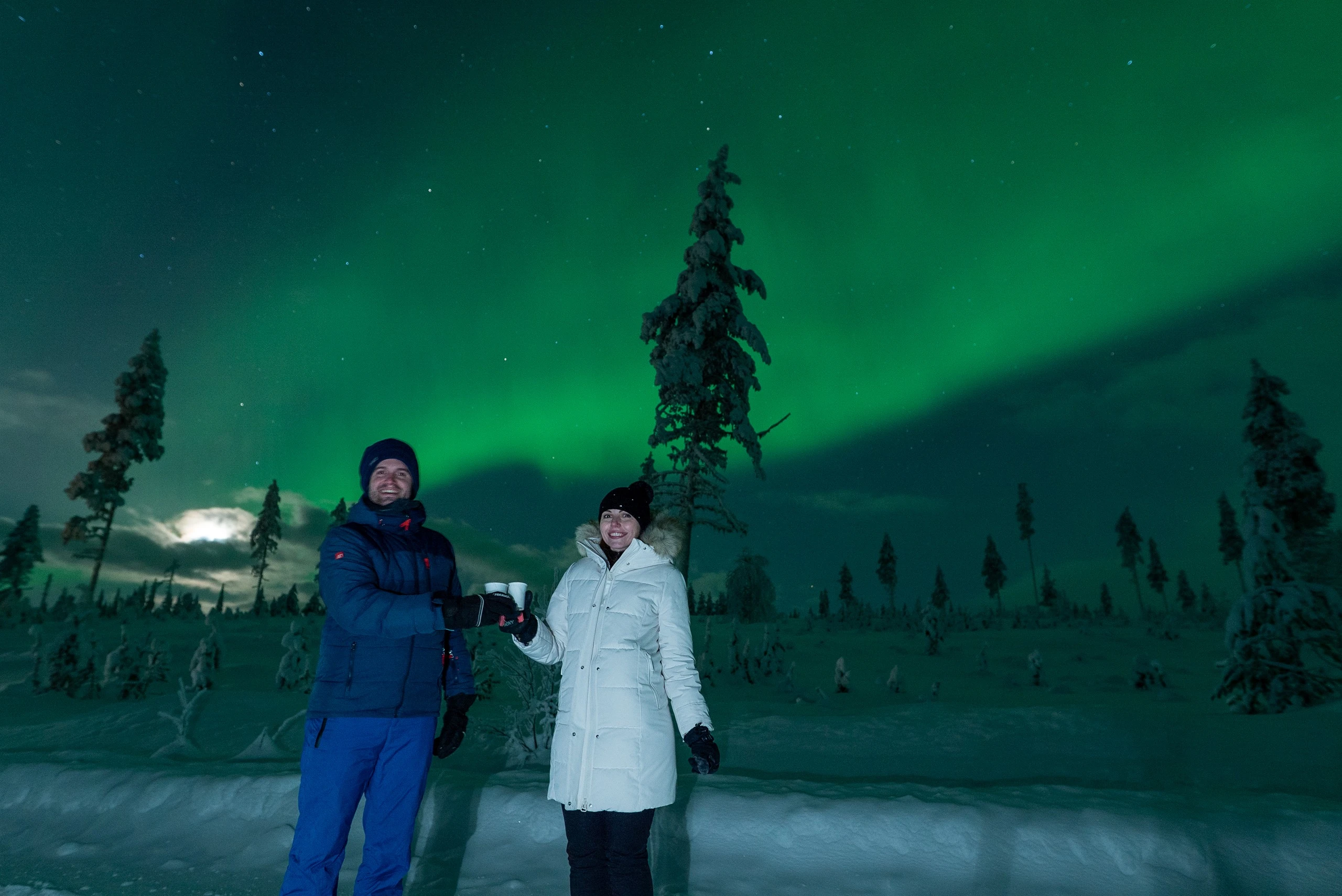 Two guests raising their cups under the northern lights