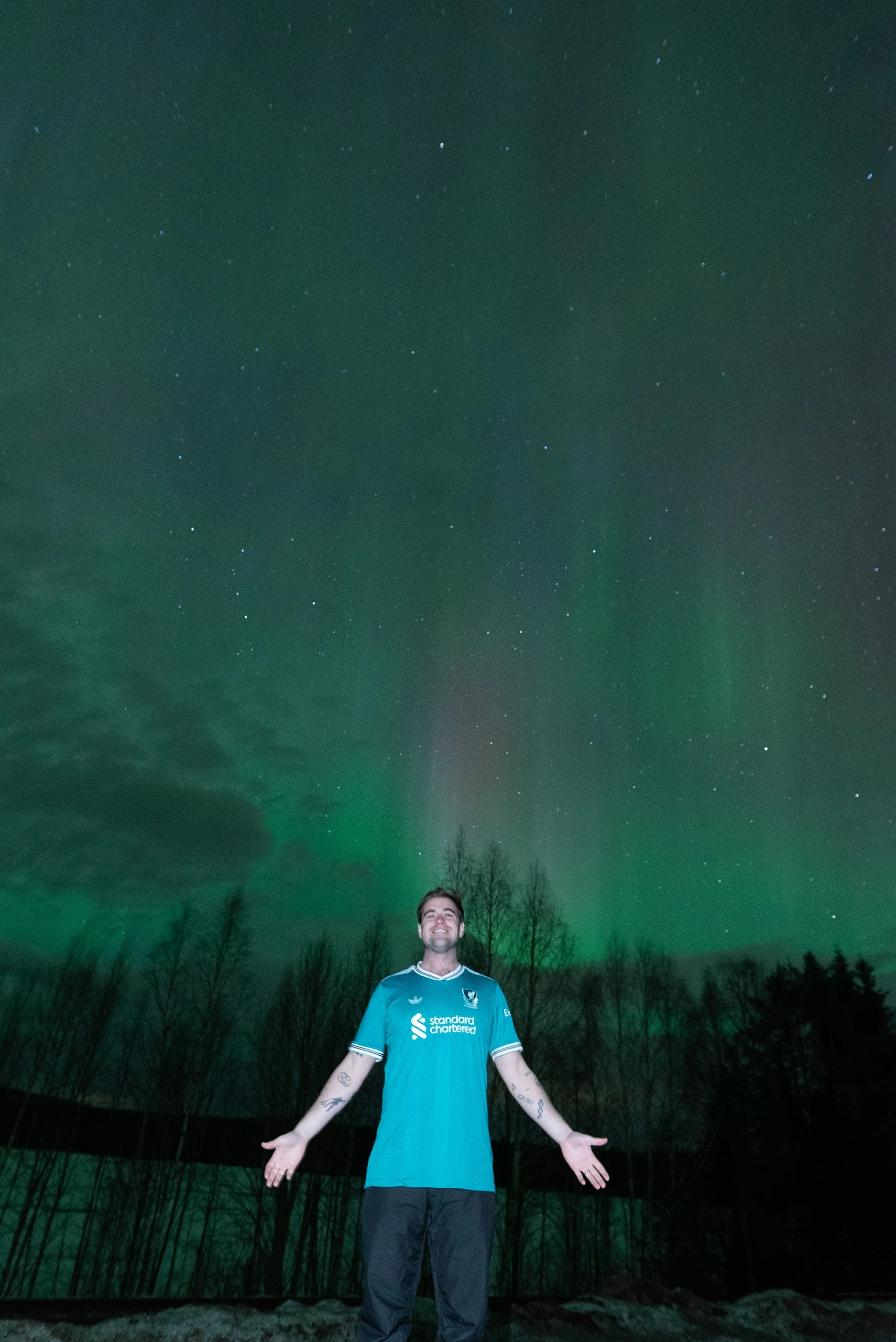 Guest with arms wide open under northern lights pillars