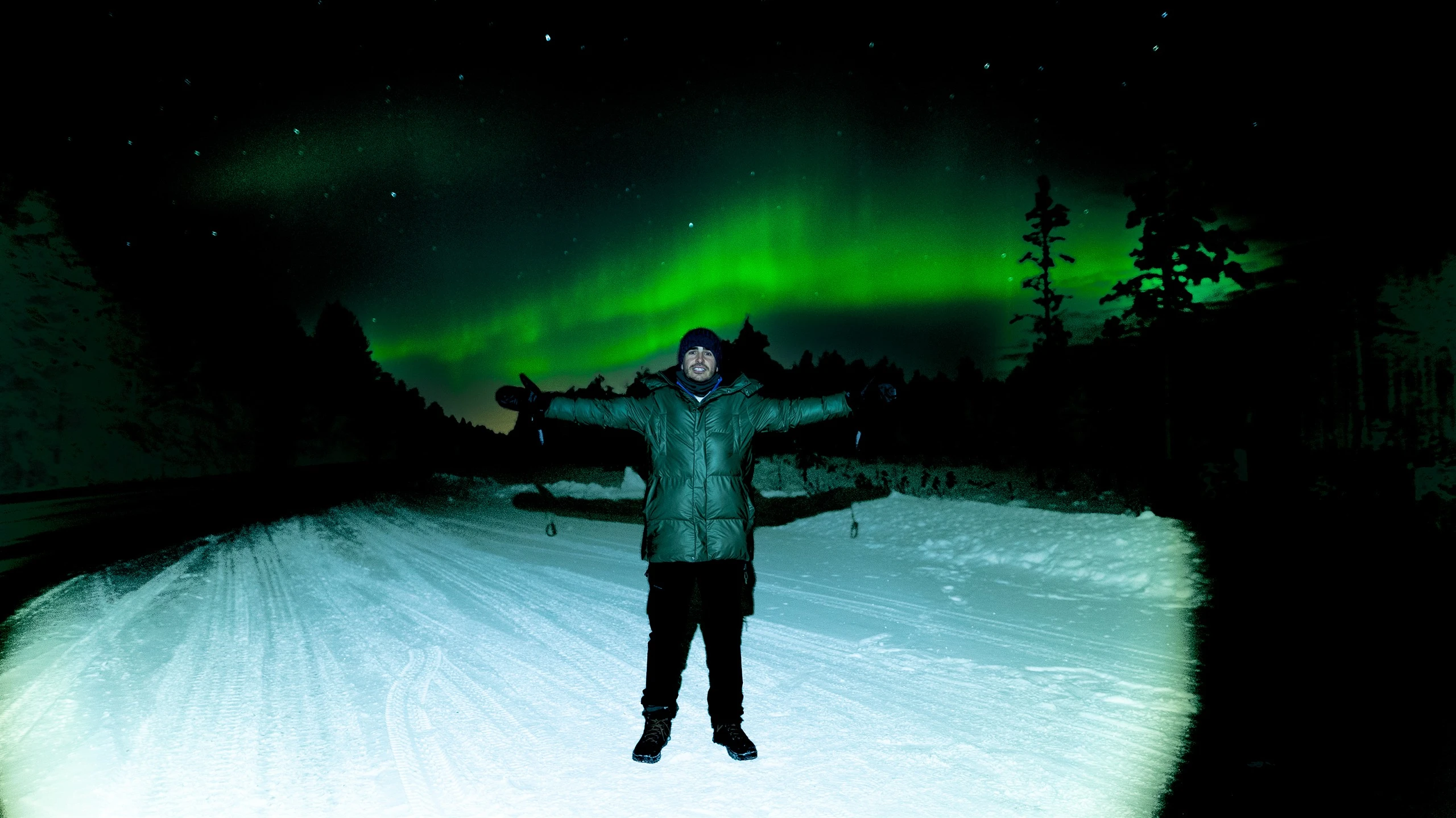 Aurora hunter standing on a snowy road under the northern lights near Levi