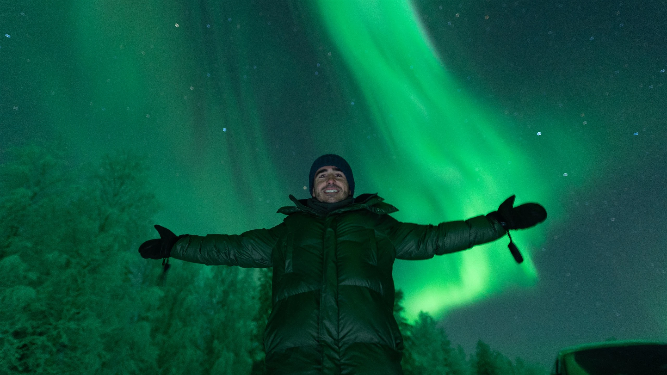 Guest with arms wide open under a strong aurora on a northern lights tour